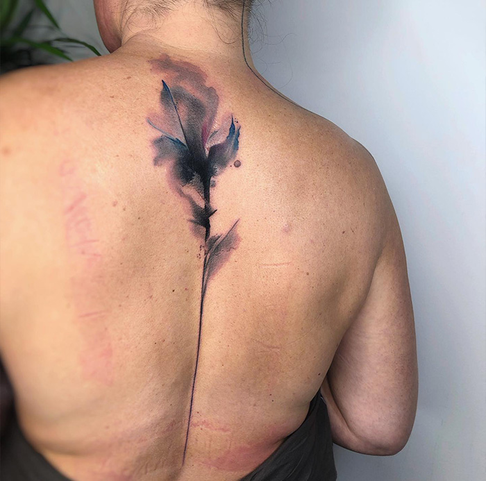 Watercolor spine tattoo design with black and pink hues on a woman's back.