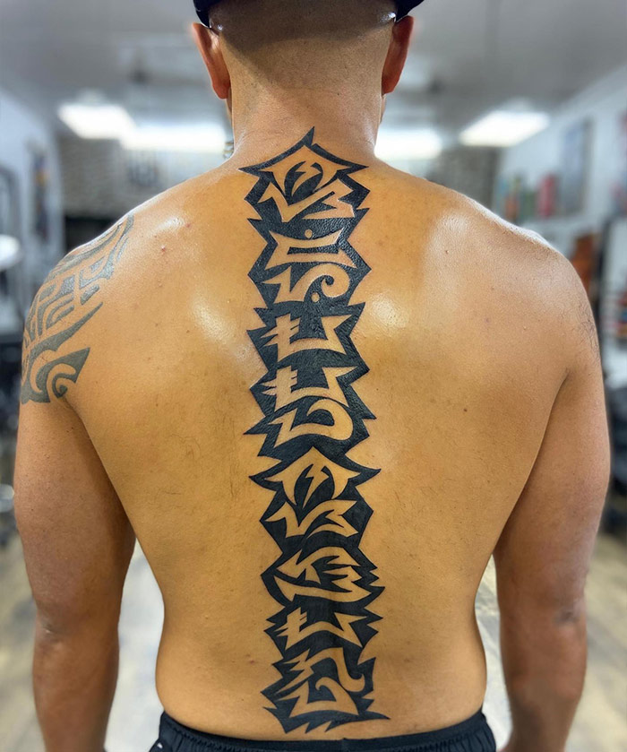 Bold, elegant spine tattoo design on a man's back, showcasing intricate patterns in black ink.