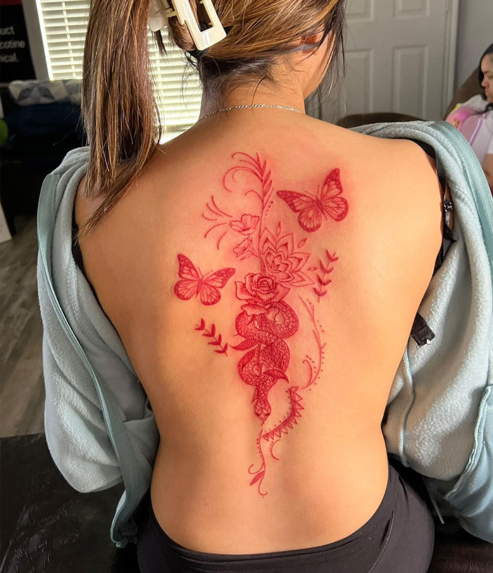 Elegant spine tattoo featuring butterflies and roses in red ink on a woman's back.