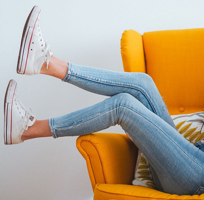 woman in blue denim jeans and white converse all star high top sneakers sitting on orange sofa