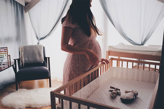 woman in a white lace sleeveless dress standing beside a brown wooden crib woman in a white lace sleeveless dress standing beside a brown wooden crib