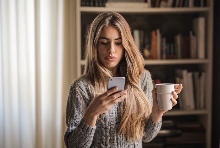 A woman checking her phone and holding a cup