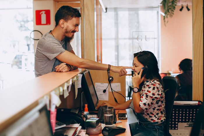 A man points at woman's nose while she is on the phone 