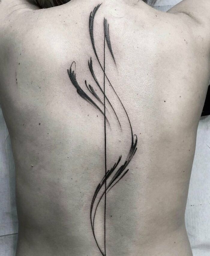 Elegant spine tattoo with abstract, flowing black lines on a person's back.