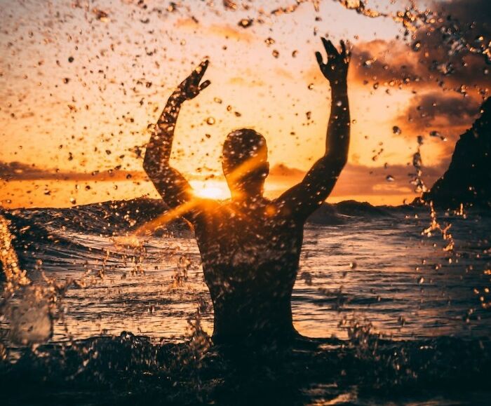 man with raised hands standing in the lake during the sunset
