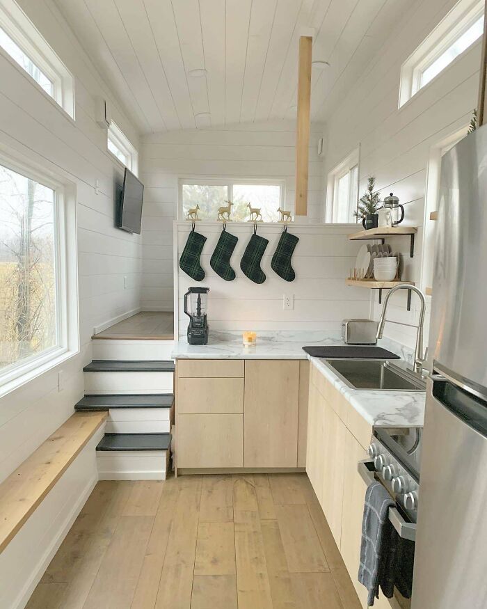 Cozy tiny house kitchen with wood accents, decorated shelves, and Christmas stockings hung above the counter.
