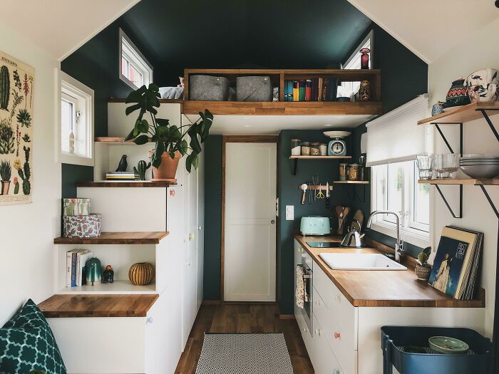 Stylish and cozy tiny house interior with kitchen, shelves, plants, and loft space.
