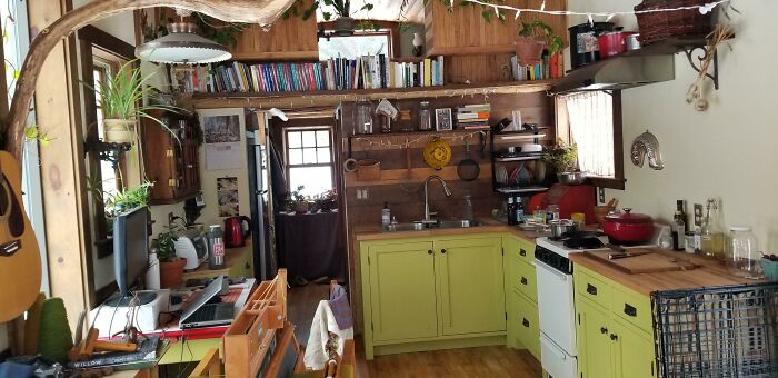 Green kitchen cabinets with wooden countertops in a cozy tiny house design featuring rustic wood walls and open shelving.