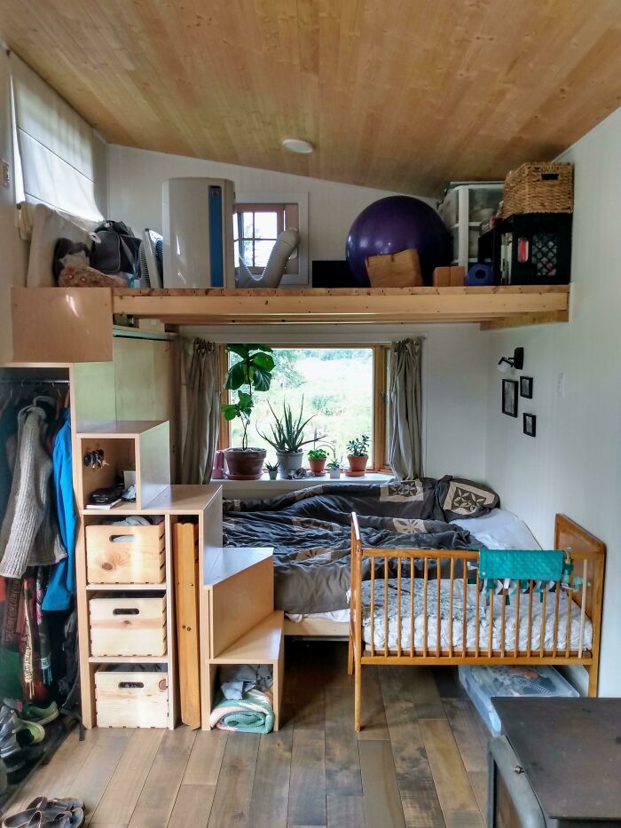 Cozy tiny house interior with loft storage, wood accents, and plants by the window.