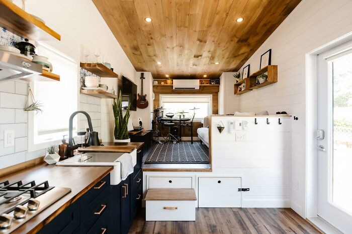 Modern white kitchen with black cabinets in a tiny house design, featuring wood accents and compact, efficient layout.