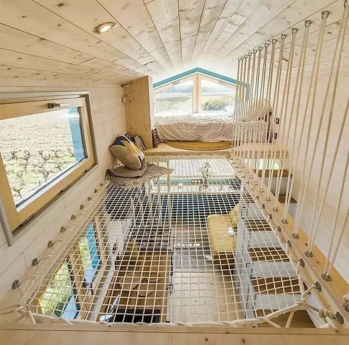 Cozy tiny house design featuring a netted loft area with pillows and a bed, showcasing innovative and irresistible architecture.