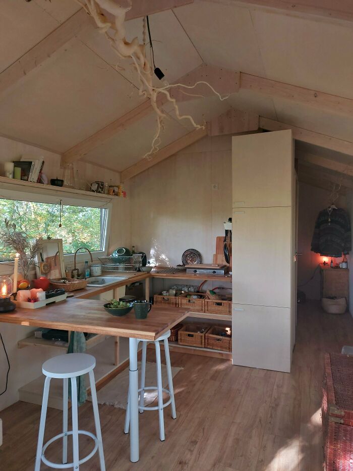 Cozy tiny house kitchen with wooden countertops, stools, open shelving, and natural light.