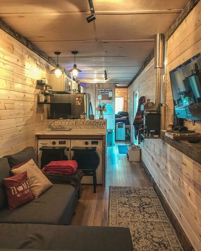 Grey couch with pillows next to laundry appliances in a cozy wood-paneled tiny house design interior.