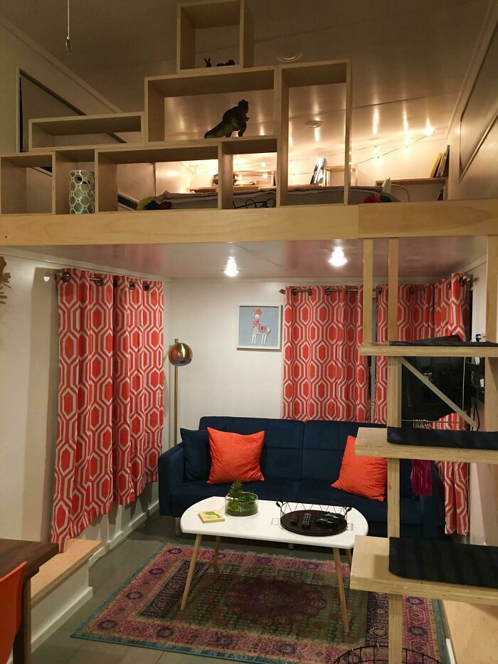 Cozy tiny house interior with a dark couch, orange pillows, patterned curtains, and a compact living space design.