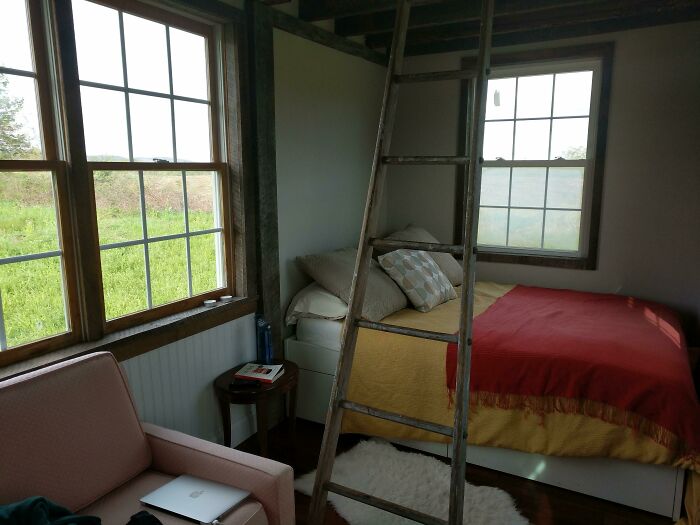 Cozy bed with yellow and red blankets in a tiny house design featuring natural light and rustic wooden ladder interior.