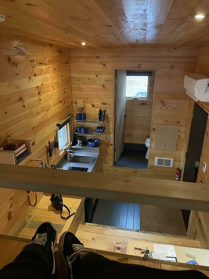Cozy tiny house interior with wood paneling, a compact kitchen, and a small bathroom viewed from an upper loft.