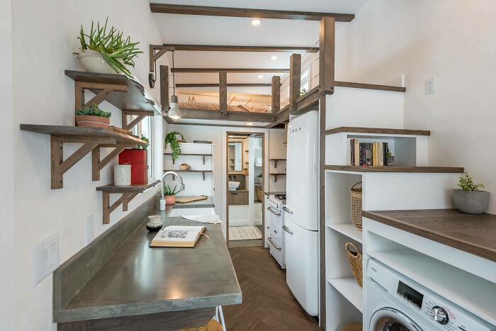 Stylish tiny house interior with loft bed, modern kitchen, and white appliances.
