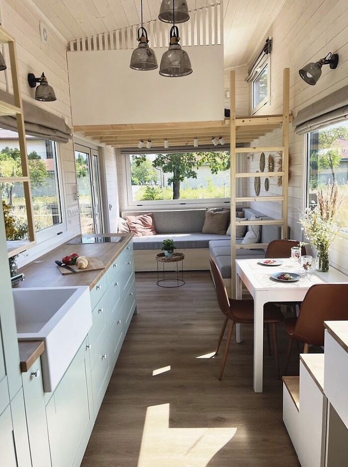 Modern tiny house design featuring big wide windows, a cozy seating area, and a bright, open kitchen and dining space.