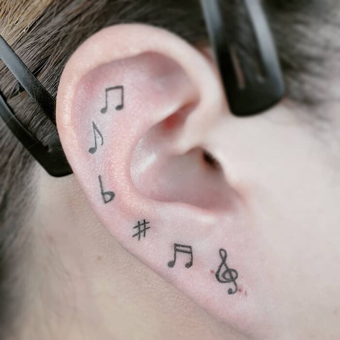Black small musical notes tattoo on ear