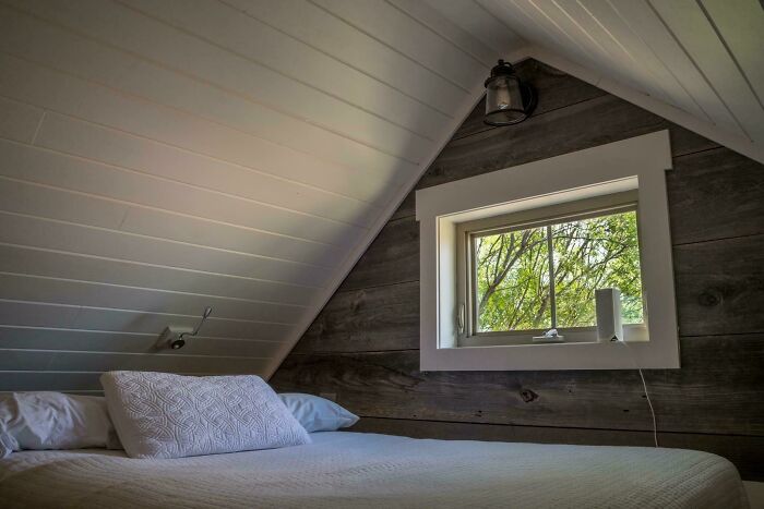 Cozy tiny house bedroom interior with wood paneling and window view.