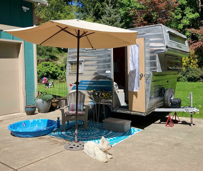 Tiny house design with a retro trailer, patio setup, umbrella, and a dog lounging on a sunny day.