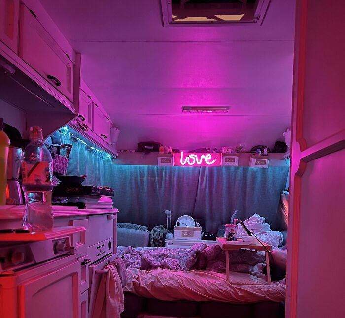 Cozy tiny house interior with neon "love" sign, pink lighting, and a comfy bed setup.