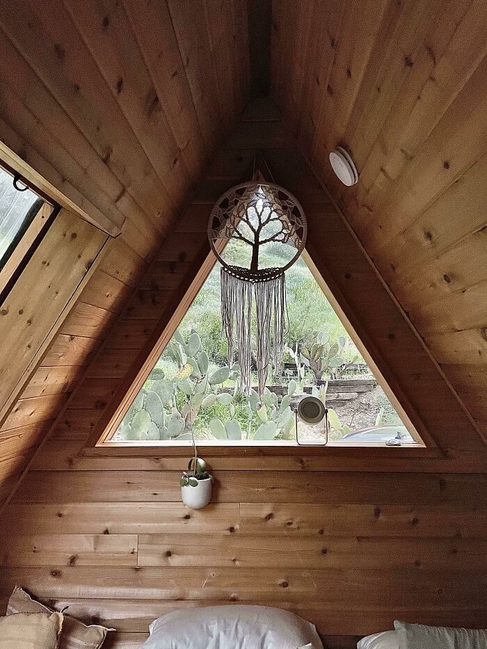 Cozy A-frame interior with wooden walls, showcasing tiny house design charm through a large triangular window and decor.