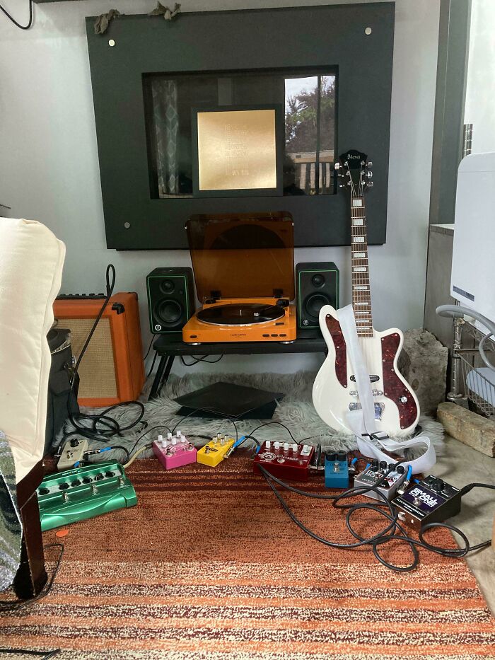 Tiny house interior with a white guitar, record player, and colorful pedals on a striped rug.