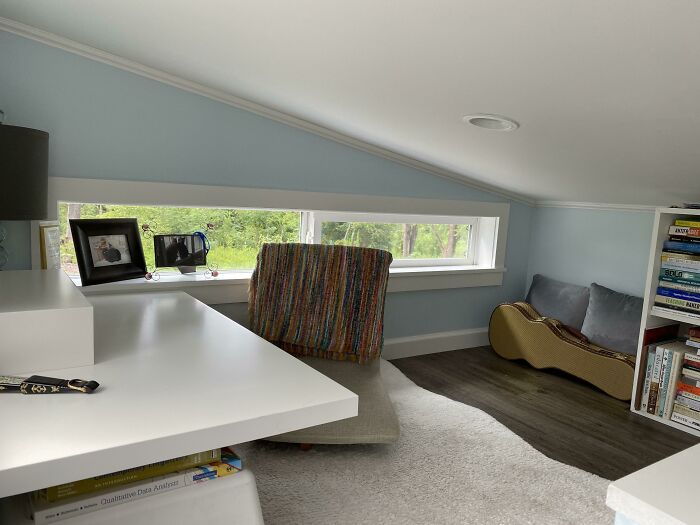 Cozy tiny house interior with a white desk, colorful chair, and low window view of greenery.