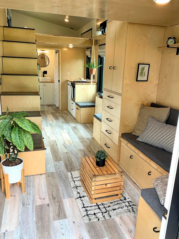 Cozy brown tiny house interior with wooden stairs, built-in seating, storage cabinets, and modern flooring design.