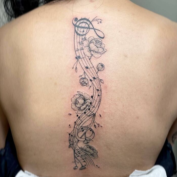 Black spine tattoo with flowers and musical notes