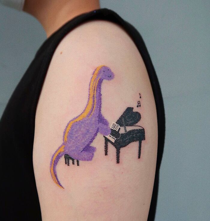 Tattoo on a shoulder of a purple dinosaur playing piano