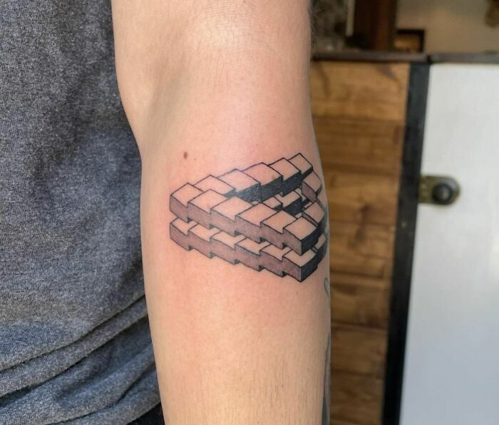 Optical illusion tattoo of interlocking cubes on person's arm.
