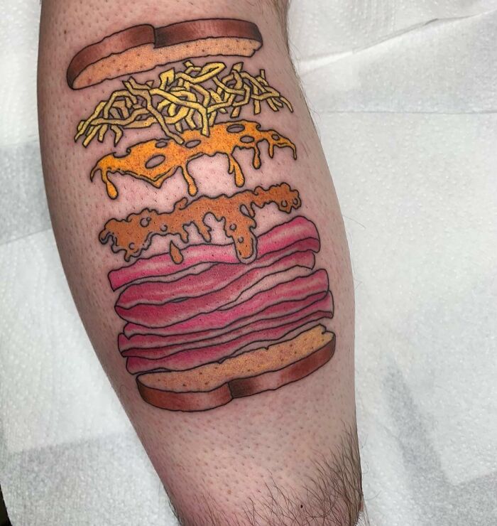 Food tattoo featuring a watercolor burger design with colorful layers on the skin.