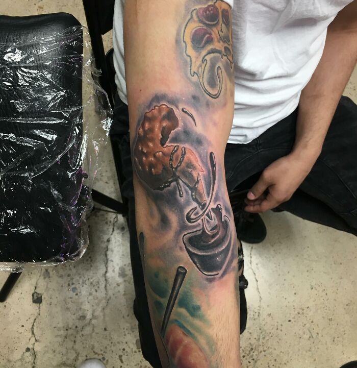 Watercolor tattoo of a chicken wing with barbecue sauce on an arm, showcasing food-inspired ink.
