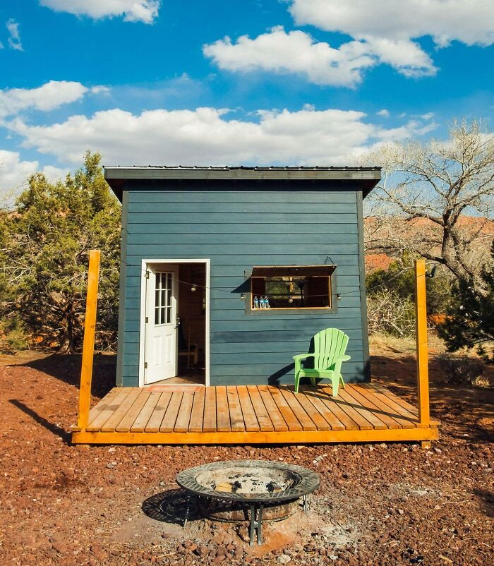 Small green tiny house with white doors and wooden deck in a natural setting, showcasing tiny house design inspiration.