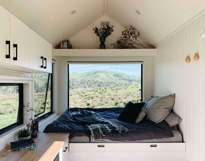 Cozy tiny house interior with white walls and wide window showcasing scenic green hills design.