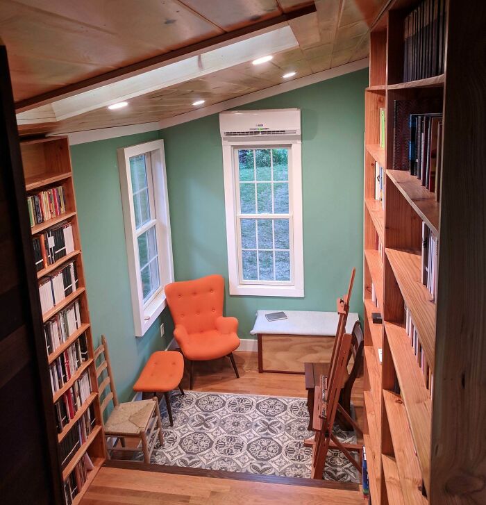 Cozy tiny house design featuring a green room with an orange chair, wooden bookshelves, and natural light from windows.