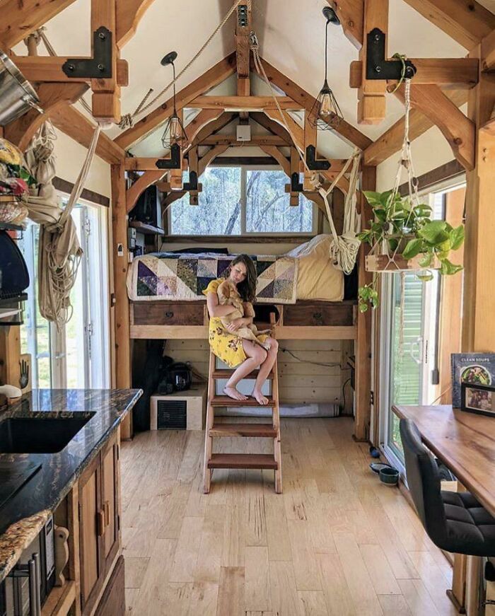 Woman hugging a dog inside a cozy tiny house with wooden beams and natural light, showcasing tiny house designs inspiration.