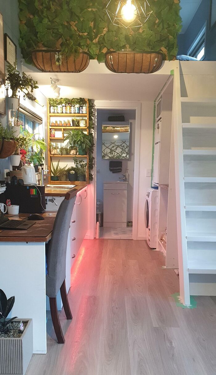 Bright white kitchen in a tiny house design featuring hanging plants, wooden countertops, and cozy compact living space.