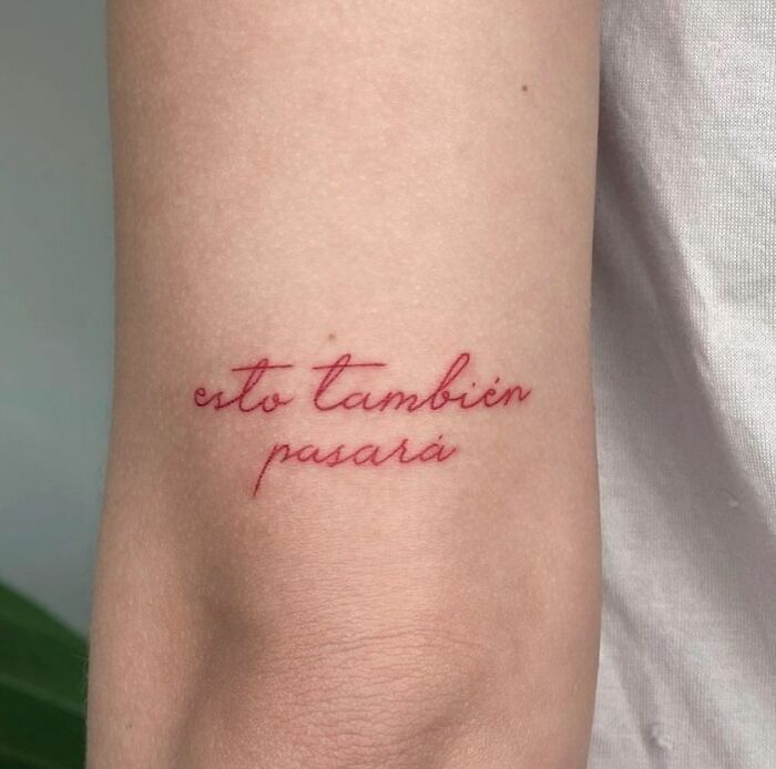 Red ink tattoo on forearm with "esto también pasará" phrase in elegant script.