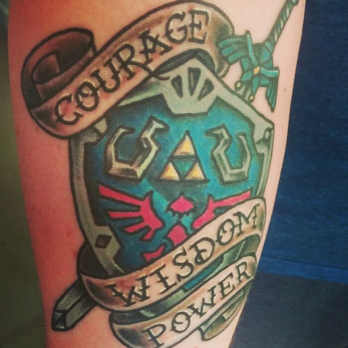 Colorful American traditional tattoo featuring a shield with banners reading "Courage," "Wisdom," "Power."