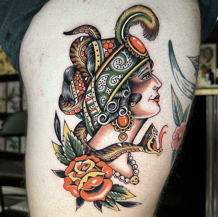 American traditional tattoo featuring an ornate g***y woman with feathers and flowers, showcasing classic bold colors and patterns.