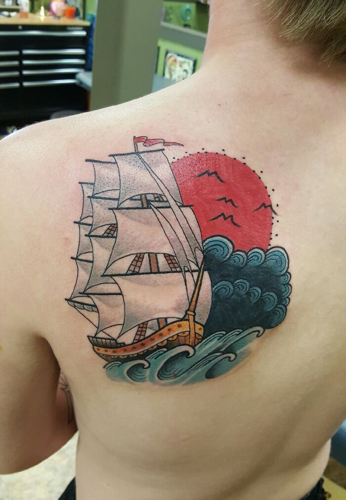 American traditional tattoo of a sailing ship and red sun on a person's back.