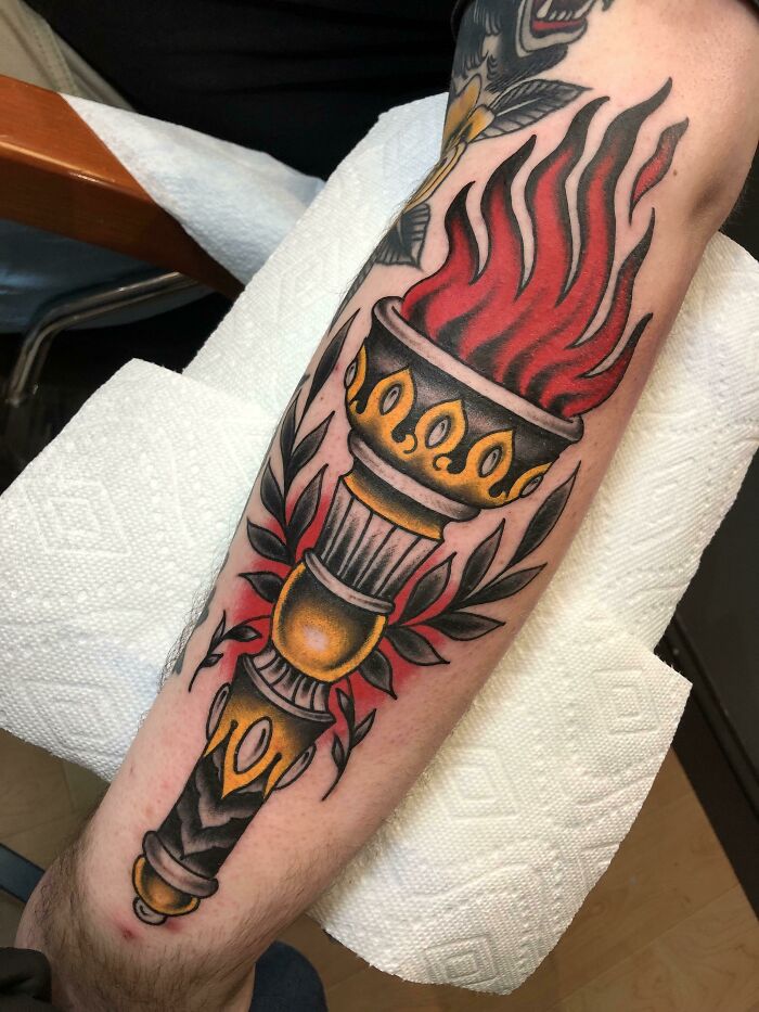 American traditional tattoo of a flaming torch with leaves on an arm, showcasing bold colors and classic design elements.