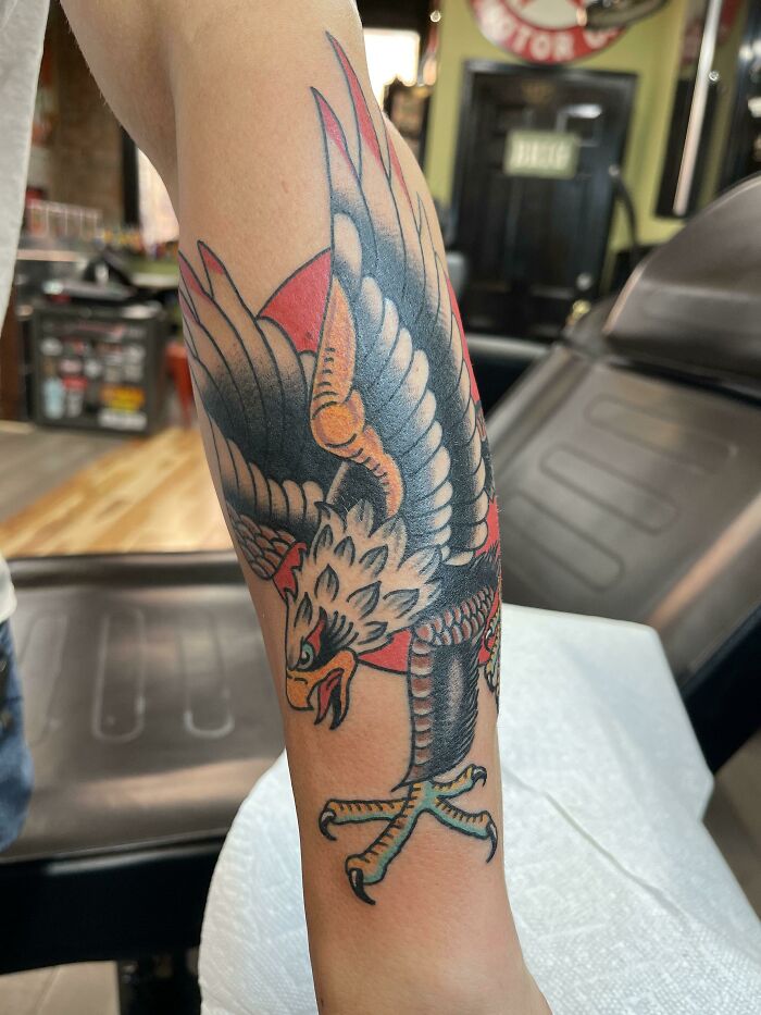 American traditional tattoo of an eagle on a forearm, showcasing bold colors and classic design in a tattoo studio setting.
