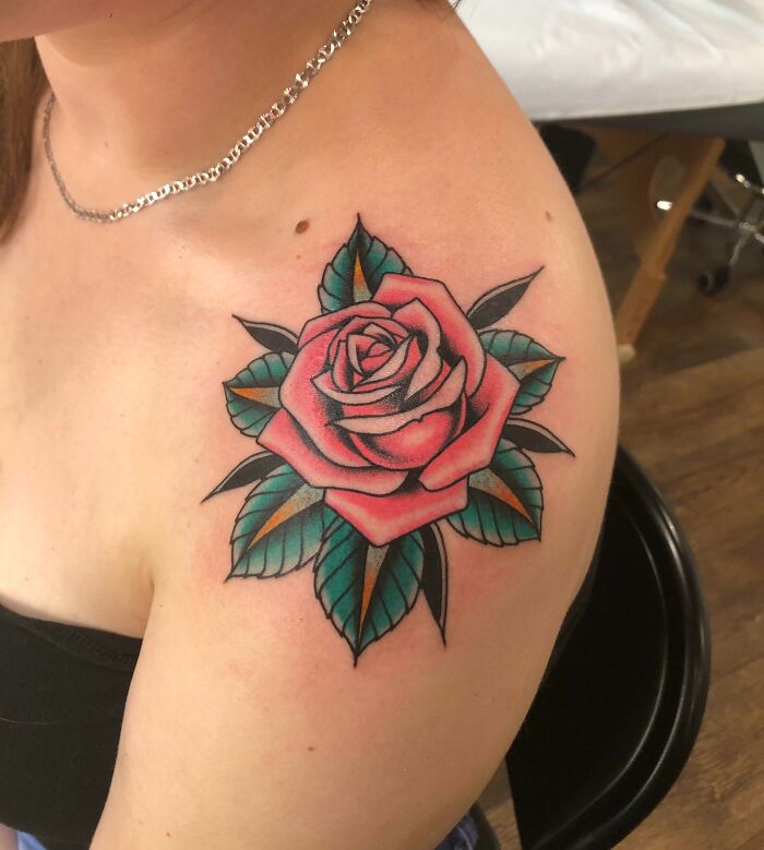 American traditional tattoo of a red rose with green leaves on a person's shoulder.