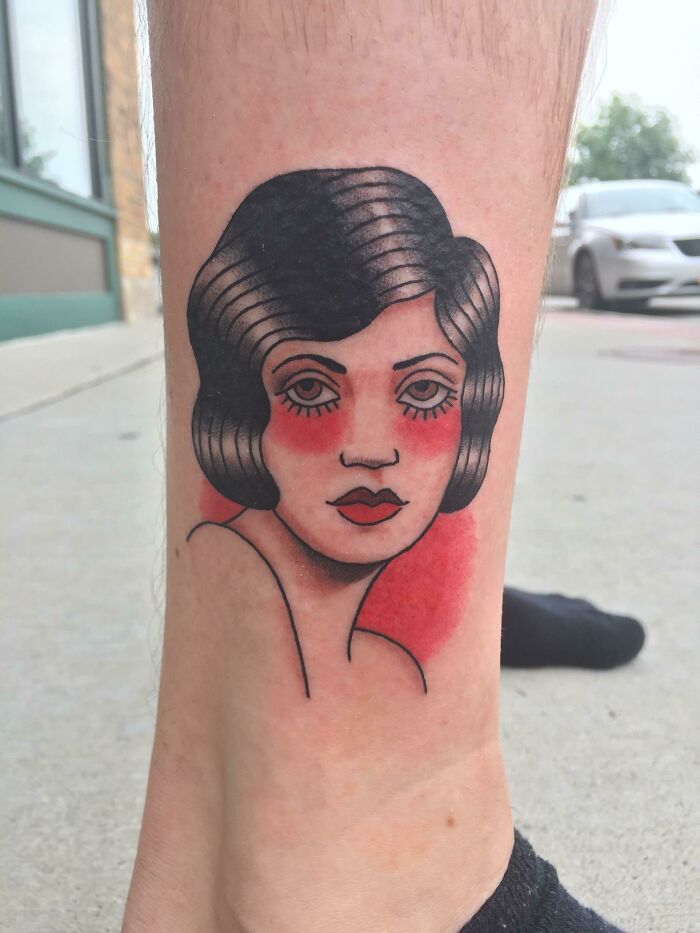 American traditional tattoo of a woman's face with bold red and black shading on the leg.