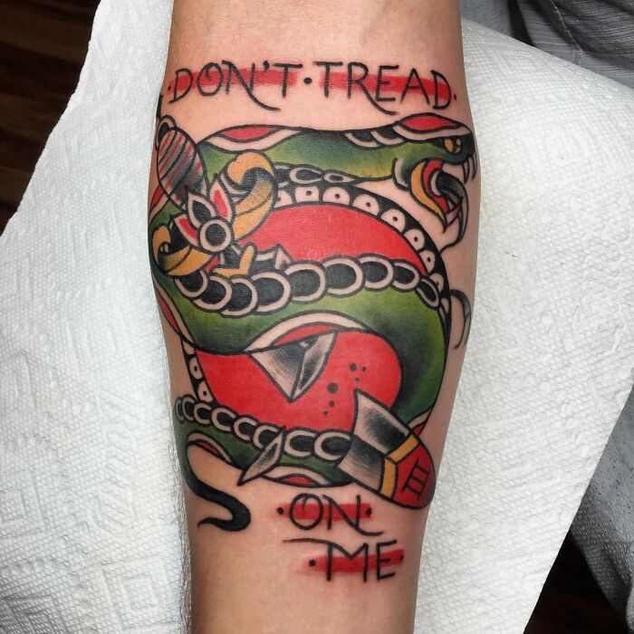 American traditional tattoo of a coiled snake with "Don't Tread On Me" text, featuring bold colors and striking design.