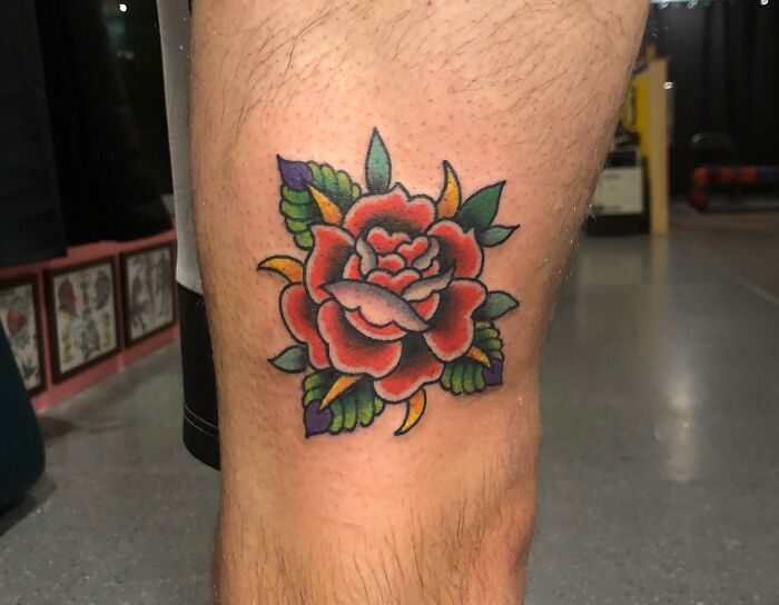 American traditional tattoo of a vibrant red rose with green leaves on a person's leg.